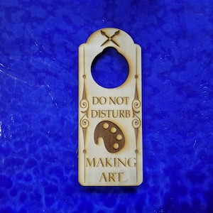 Könnte beinhalten: Ein hölzerner Türhänger mit dem Text "Nicht stören, Kunst machen" und einem bemalten Paletten-Design.