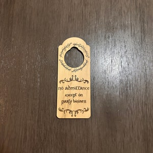 以下が含まれることがあります： エルフ語で書かれた円形の碑文が刻まれた木製ドアハンガー。碑文には「一つの指輪、すべてを支配する、一つの指輪、すべてを見つける、一つの指輪、すべてを連れてくる、そして闇の中で縛る」と書かれています。碑文の下には「パーティーの用事以外は立ち入り禁止」という文が書かれています。