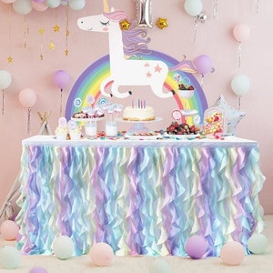 May include: A pastel rainbow table skirt with ruffles, perfect for a unicorn-themed party. The skirt is made of soft, flowing fabric and is decorated with a unicorn and rainbow design.