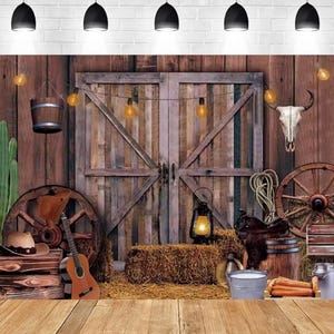 Puede incluir: Un telón de fondo rústico con temática del oeste con una puerta de granero de madera, ruedas de carro y una calavera de vaca. La escena incluye una guitarra, una paca de heno y una linterna, creando una estética campestre vintage.