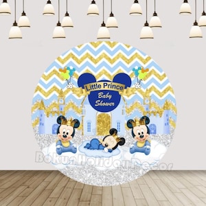 May include: A blue and gold baby shower backdrop with a chevron pattern. The backdrop features a castle, clouds, and two Mickey Mouse characters wearing crowns. The text "Little Prince Baby Shower" is displayed in a blue banner.