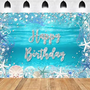 Puede incluir: Un telón de fondo turquesa con un mensaje de Feliz Cumpleaños en escritura plateada. El diseño presenta estrellas de mar, conchas marinas, perlas y detalles brillantes. El fondo tiene un tema submarino.