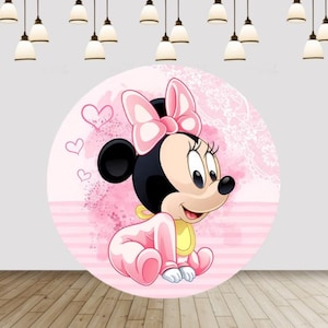 Puede incluir: Un telón de fondo rosa redondo con una ilustración de dibujos animados de Minnie Mouse con un traje de bebé. El diseño incluye corazones rosas y un lazo. El fondo tiene un efecto acuarela y un patrón de encaje.