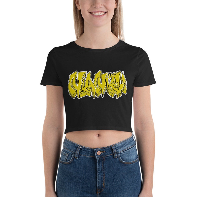 May include: Black crop top with the word "WAVE" in yellow graffiti-style lettering. The word is outlined in black and has a 3D effect. The shirt is made of a soft material.
