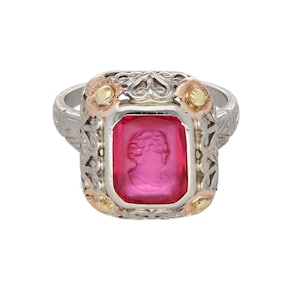 Puede incluir: Un anillo de plata con una piedra preciosa rosa rectangular con un perfil tallado. El anillo tiene detalles ornamentados y acentos de oro y oro rosa. El diseño incluye elementos florales y una banda detallada.
