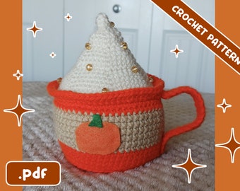 May include: A crocheted mug with a whipped cream topping, adorned with gold beads. The mug is orange, tan, and white, with a felt pumpkin applique. The image includes the text "CROCHET PATTERN" and ".pdf".