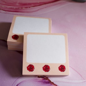 May include: A stack of pink and white notepad paper with a rose design. The notepad paper is blank and ready to be written on.