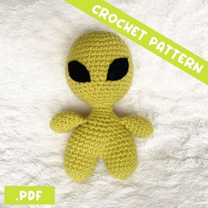 May include: A crochet pattern for a green alien amigurumi toy. The pattern is available as a PDF download. CROCHET PATTERN is written in green letters on a yellow background.
