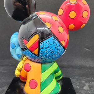 K&ouml;nnte beinhalten: Eine farbenfrohe, vielseitige Figur von Mickey Mouse. Die Figur ist aus bemaltem Harz gefertigt und hat ein Farbschema in Schwarz, Rot, Gelb, Blau, Gr&uuml;n und Orange. Die Figur steht auf einem schwarzen Sockel.