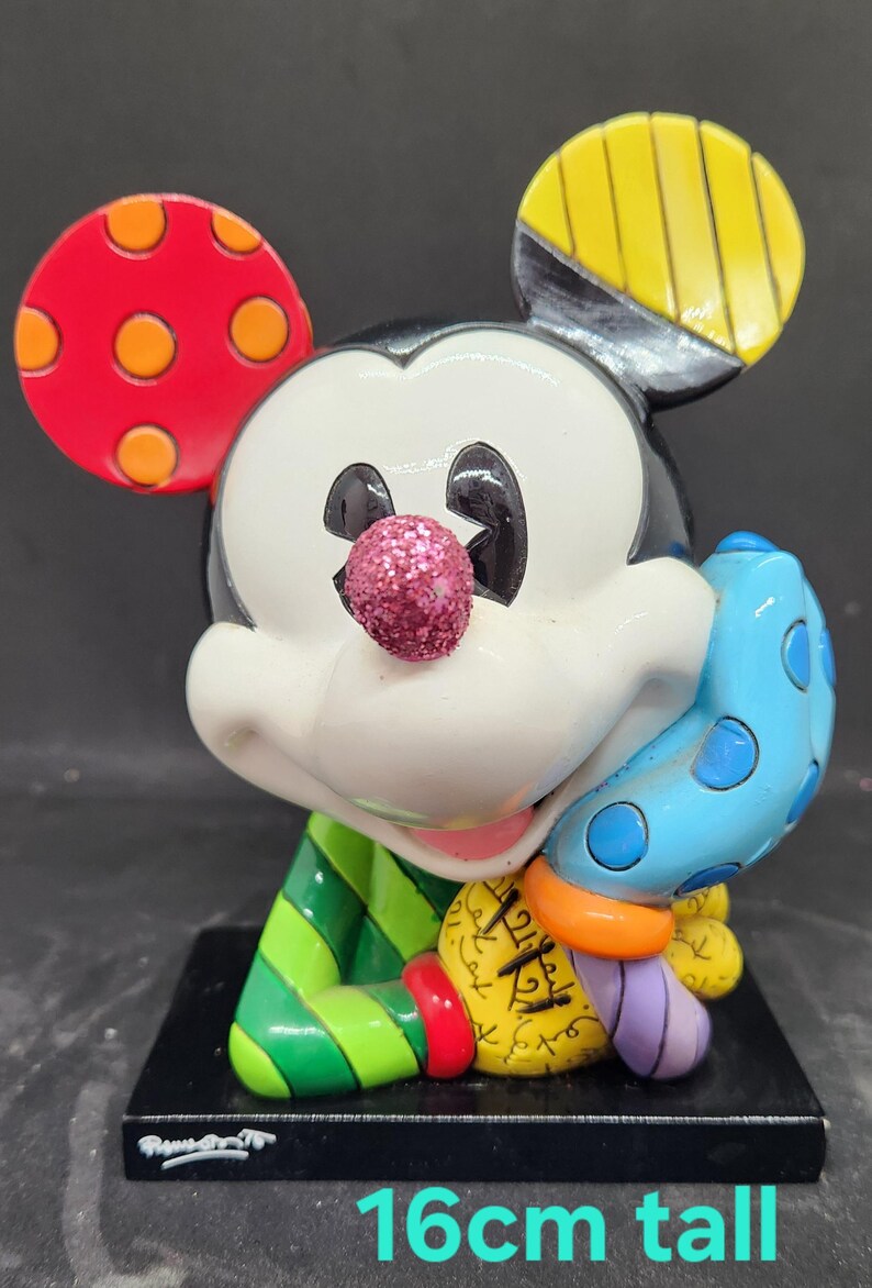 K&ouml;nnte beinhalten: Eine farbenfrohe Keramikfigur von Mickey Mouse, 16 cm hoch. Mickey tr&auml;gt ein gr&uuml;n-gelb gestreiftes Hemd und eine blau-wei&szlig; gepunktete M&uuml;tze. In seiner rechten Hand h&auml;lt er einen blau-wei&szlig; gepunkteten Handschuh.