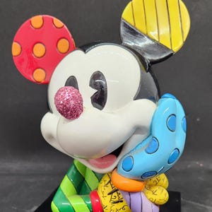K&ouml;nnte beinhalten: Eine farbenfrohe, stilisierte Figur von Mickey Mouse mit einer pinkfarbenen Glitzernase. Er tr&auml;gt ein gr&uuml;n-rot gestreiftes Hemd und einen blauen Handschuh mit wei&szlig;en Punkten. Die Figur steht auf einem schwarzen Sockel mit der Unterschrift des K&uuml;nstlers.