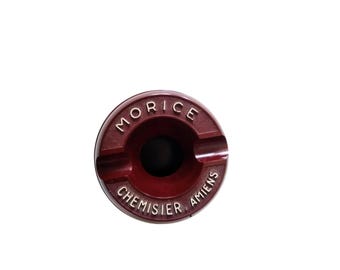 Peut inclure: Un cendrier rond rouge avec le texte "MORICE CHEMISIER AMIENS" en lettres blanches.