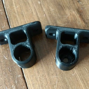May include: Two black plastic wall mounts with a round hole in the center. The mounts are designed to hold a rod or pipe.