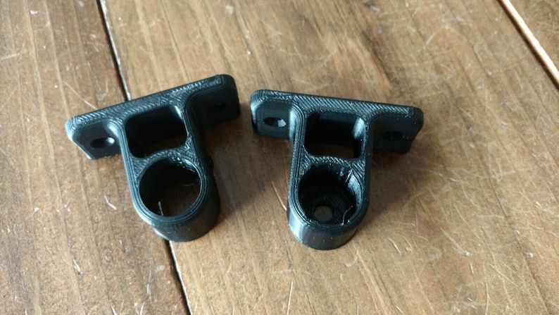 May include: Two black plastic wall mounts with a round hole in the center. The mounts are designed to hold a rod or pipe.