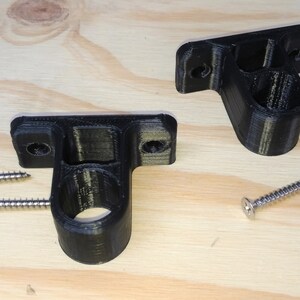 May include: Two black plastic wall mounts with a round hole in the center. The mounts are designed to hold a rod or pipe. Four silver screws are included.