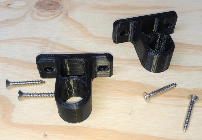 May include: Two black plastic wall mounts with a round hole in the center. The mounts are designed to hold a rod or pipe. Four silver screws are included.