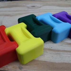 May include: Five brightly coloured, T-shaped objects in red, yellow, green, blue, and purple. Each has a rectangular base and a handle-like top. They are arranged on a light brown wooden surface.