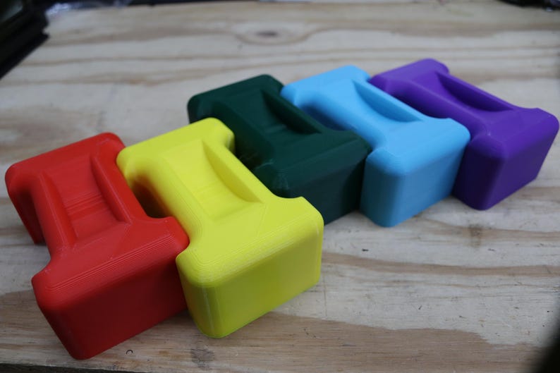 May include: Five brightly coloured, T-shaped objects in red, yellow, green, blue, and purple. Each has a rectangular base and a handle-like top. They are arranged on a light brown wooden surface.