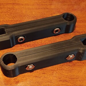 May include: Two black plastic 3D printed parts with holes and screw heads. The parts are designed to be joined together.