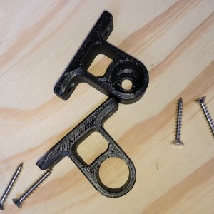 May include: Two black plastic brackets with round holes and a flat surface. Four silver screws are scattered on a wooden surface.