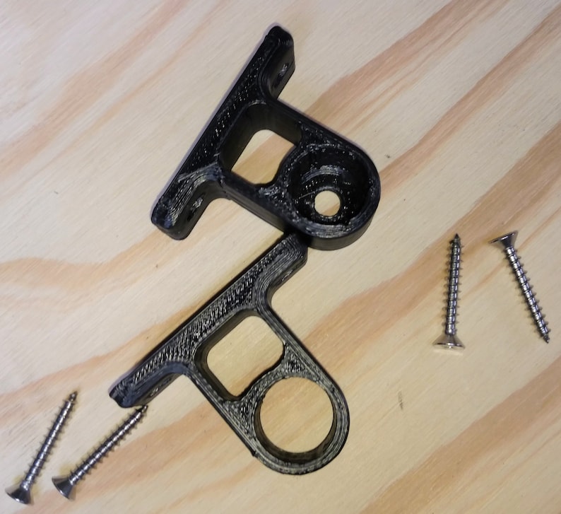 May include: Two black plastic brackets with round holes and a flat surface. Four silver screws are scattered on a wooden surface.
