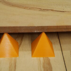 May include: Two orange, pyramid-shaped supports holding up a wooden board. The supports are made of a solid material and are evenly spaced. The wood grain is visible on the board and the surface it rests on.