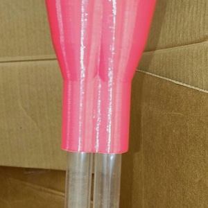 May include: A pink plastic funnel attached to two clear plastic tubes. The tubes are connected by a black plastic connector.