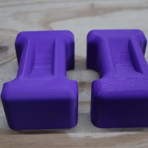 May include: Two purple, rectangular objects with a T-shaped design. The objects have a textured surface and are placed side by side. The background is a light brown wooden surface.