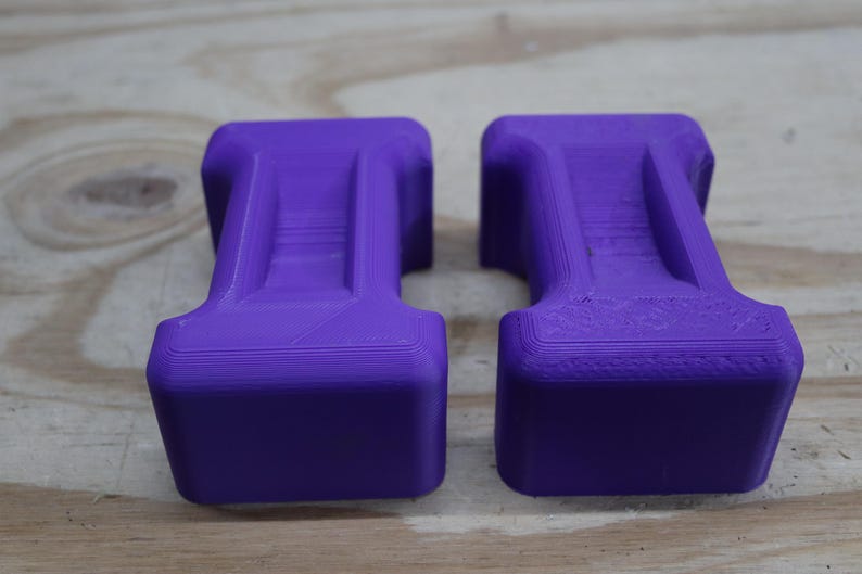 May include: Two purple, rectangular objects with a T-shaped design. The objects have a textured surface and are placed side by side. The background is a light brown wooden surface.