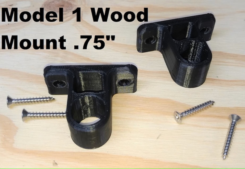 May include: Two black plastic wall mounts with screw holes and a 0.75 inch diameter hole. The mounts are on a wooden surface with four silver screws.