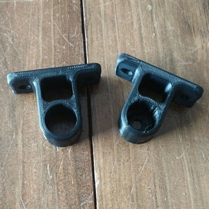 May include: Two black plastic wall mounts with a round hole in the center. The mounts are designed to hold a rod or pipe.