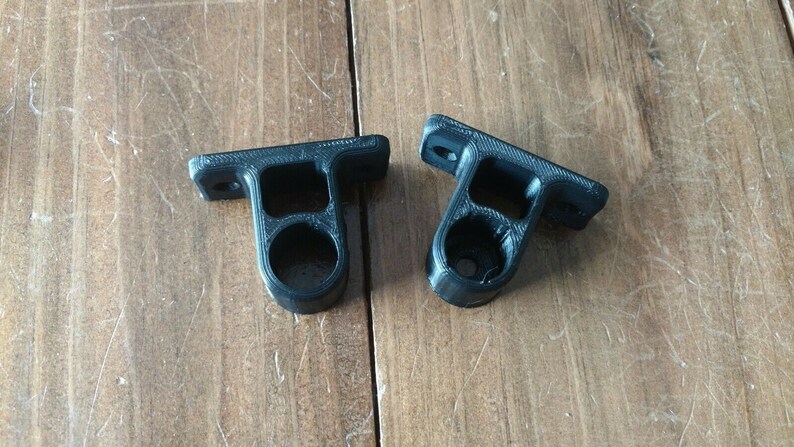 May include: Two black plastic wall mounts with a round hole in the center. The mounts are designed to hold a rod or pipe.