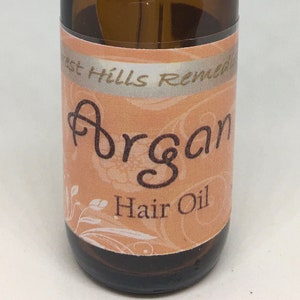 May include: A brown glass bottle with a black dropper top and a label that says "Forest Hills Remedies Argan Hair Oil".