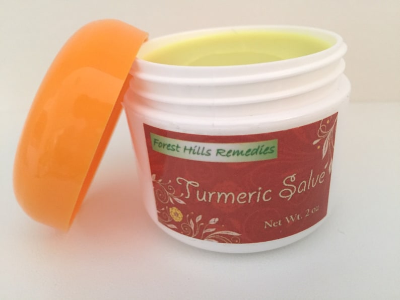 K&ouml;nnte beinhalten: Ein kleines wei&szlig;es Glas mit orangefarbenem Deckel, gef&uuml;llt mit einer gelben Salbe. Das Glas hat ein rotes Etikett mit dem Text "Forest Hills Remedies Turmeric Salve Net Wt. 2 oz."