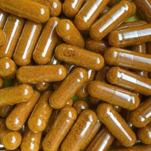 May include: A close-up image of a pile of clear capsules filled with a yellow-orange powder. The capsules are arranged in a random pattern, with some overlapping.
