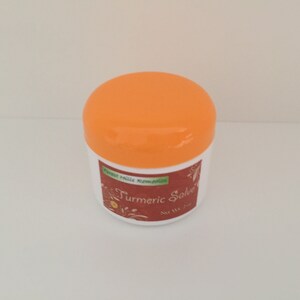 K&ouml;nnte beinhalten: Ein wei&szlig;es Glas mit einem orangenen Deckel. Das Glas ist mit "Turmeric Salve" beschriftet, &uuml;ber dem Etikett steht "Forest Hills Remedies".
