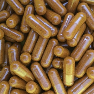 May include: A close-up image of a pile of brown capsules. The capsules are clear and filled with a brown powder.