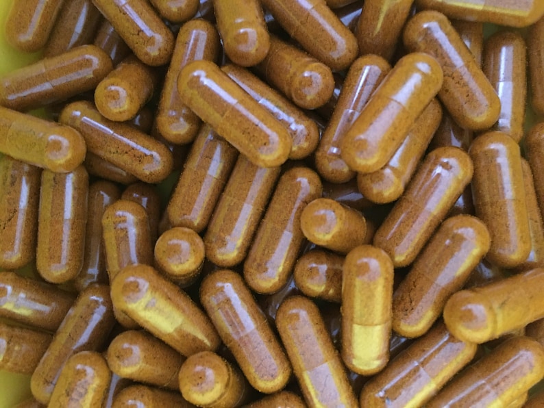 May include: A close-up image of a pile of brown capsules. The capsules are clear and filled with a brown powder.