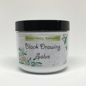 May include: A white jar with a black lid, labeled "Forest Hills Remedies Black Drawing Salve". The label has a floral design with green leaves and yellow flowers.