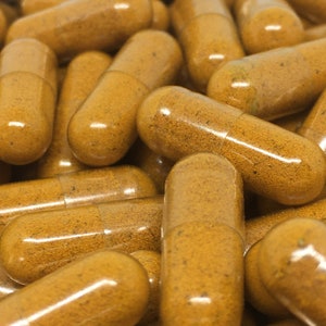 Puede incluir: Primer plano de un montón de cápsulas translúcidas llenas de un polvo naranja brillante. Las cápsulas están dispuestas en un patrón aleatorio, con algunas superpuestas.