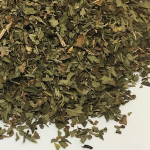 May include: A close-up of a pile of dried green mint leaves. The leaves are a mix of light and dark green, and some are slightly brown.