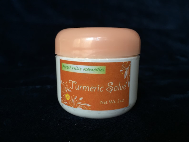 K&ouml;nnte beinhalten: Ein wei&szlig;es Glas mit einem pfirsichfarbenen Deckel und einem Etikett mit der Aufschrift "Forest Hills Remedies Turmeric Salve Net Wt. 2 oz". Das Etikett zeigt eine gelbe Blume und gr&uuml;ne Bl&auml;tter auf orangefarbenem Hintergrund.