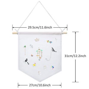 May include: White fabric jewelry organizer, 12.2 inches long and 10.6 inches wide, with a wooden dowel and hanging string. The fabric is decorated with various embroidered jewelry pieces, including a crown, a skateboard, and a cat.