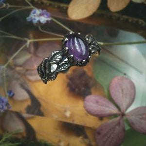 Könnte beinhalten: Ein silberner Ring mit einem violetten Amethyst-Edelstein, der in einem Blattdesign gefasst ist.
