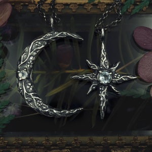 May include: Two silver necklaces with a crescent moon and a star pendant. Both pendants feature intricate floral designs and clear gemstones.