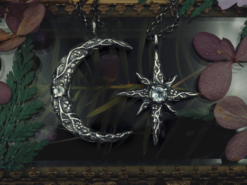 May include: Two silver necklaces with a crescent moon and a star pendant. Both pendants feature intricate floral designs and clear gemstones.