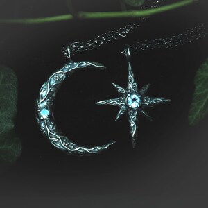 May include: Two silver necklaces with a crescent moon and a star pendant. Both pendants have a blue gemstone in the center.