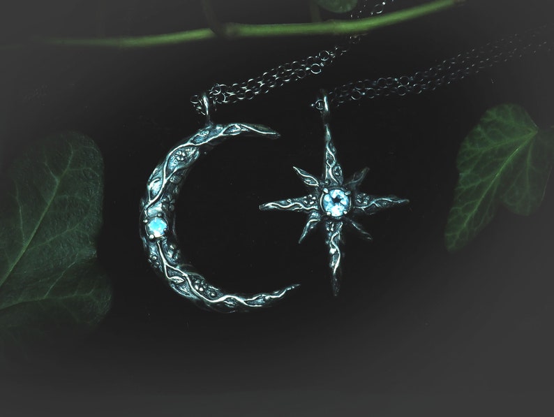 May include: Two silver necklaces with a crescent moon and a star pendant. Both pendants have a blue gemstone in the center.