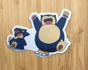 May include: A sticker featuring two blue and black Pokemon characters, Snorlax and Munchlax, with a white background. Snorlax is holding a donut in its right hand and a donut in its left hand. Munchlax is holding a donut in its mouth.