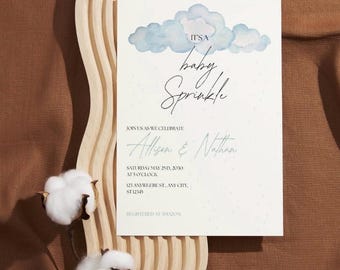 May include: A baby sprinkle invitation featuring a watercolour illustration of blue clouds. The text reads "It's a baby sprinkle" and includes the names "Allison & Nathan", the date "Saturday May 2nd, 2030", the time "at 5 o'clock", the address "123 Anywhere St, Any City, ST 12345", and the registry information "Registered at Amazon".